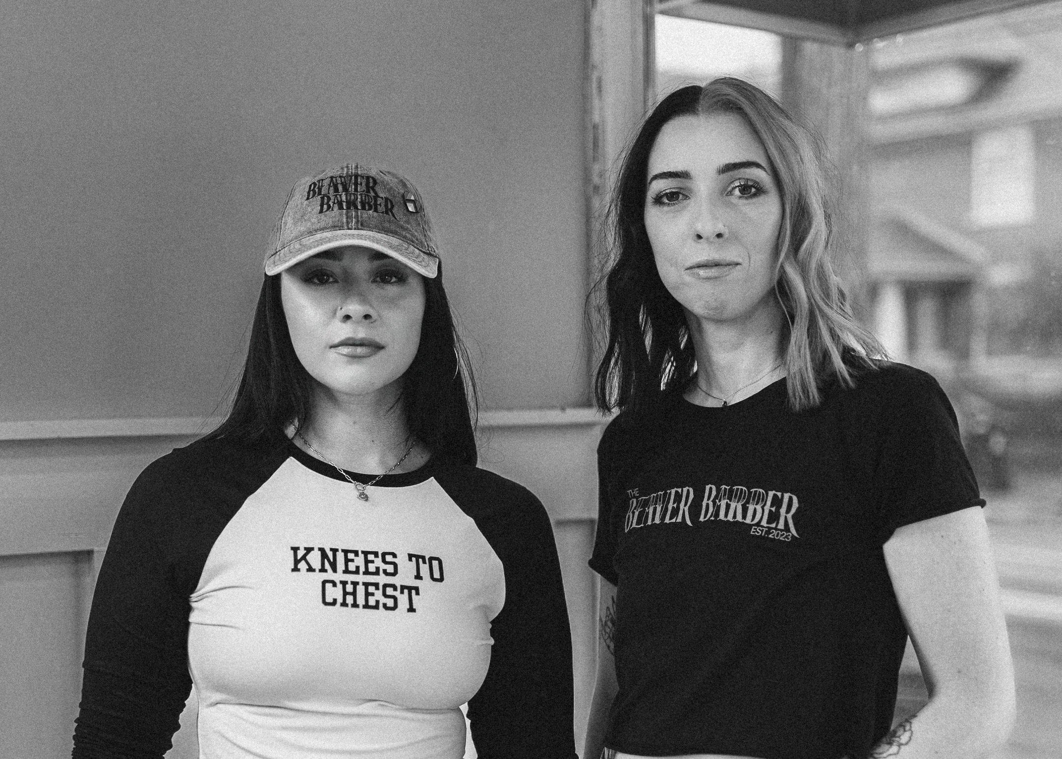 Two women standing side by side wearing casual clothing with text on their shirts.